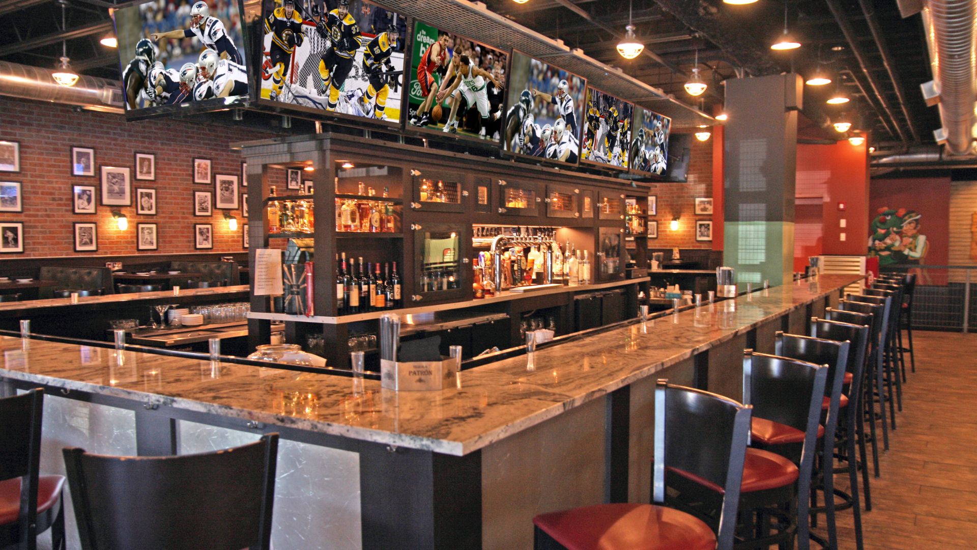 Marble bar with red and black bar stools around the perimeter in front of multiple television sets playing sports and drinks on bar at SKYBOKX 109 Sports Bar & Grill in Natick, MA